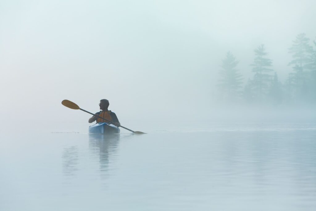 Senior solo traveling man Kayaking in dense fog in wilderness waters